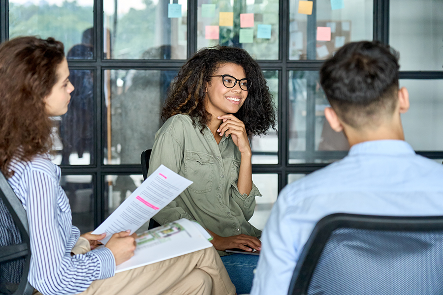 Three people in a meeting with post-it notes behind them on a glass window partition. 