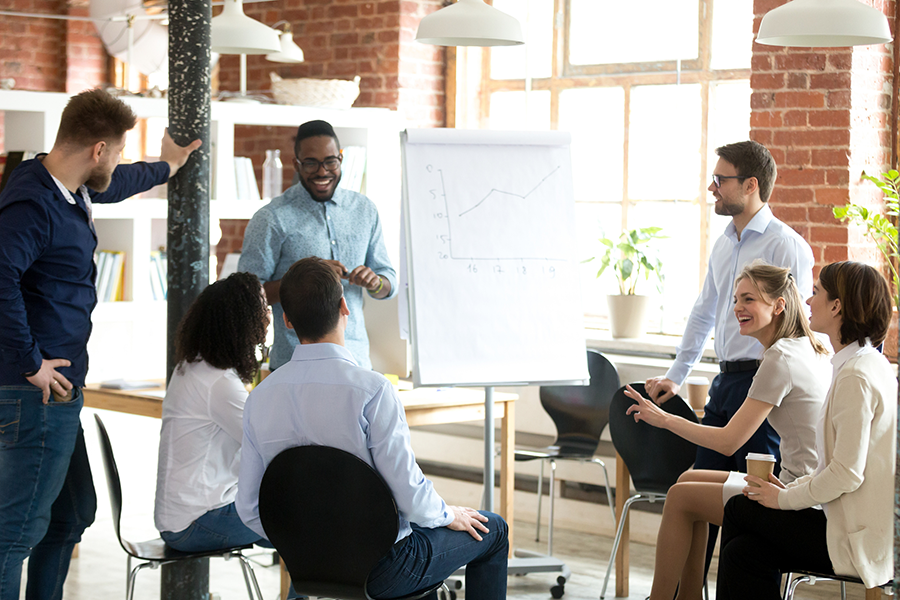 A group of people have a discussion in front of a chart in an open plan office